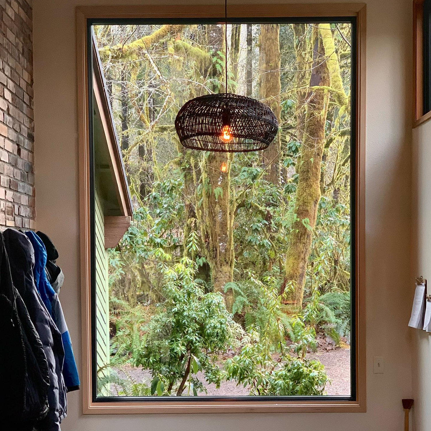 Image of a mudroom/entry way with a woven light fixture hanging from the ceiling directly in front of a large, picture window.