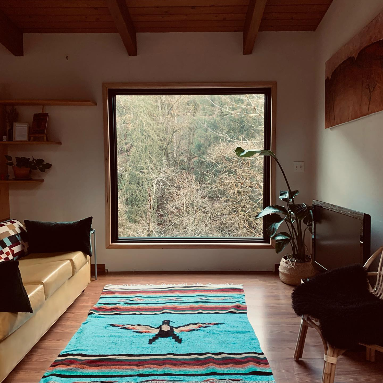 A sitting room with a turquoise, woven rug on the floor in front of a large picture window.