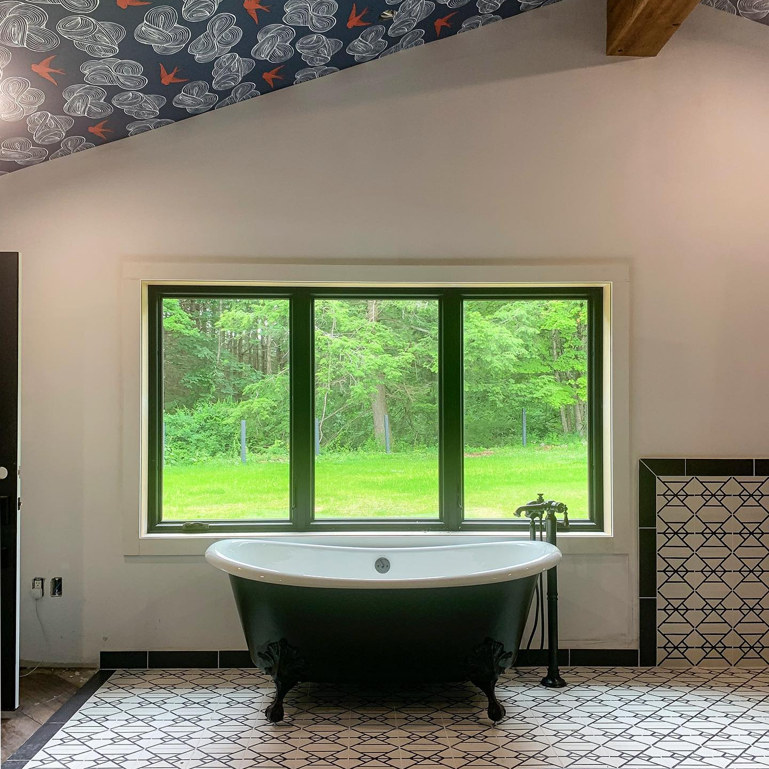 Tile bathroom with a black tub that has gliding black windows above the tub.