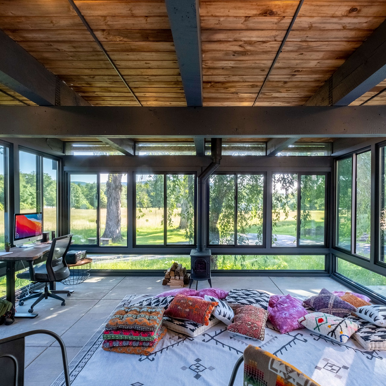 4 seasons porch/meditation studio with a wood ceiling, black windows all around, and meditation props on the floor.