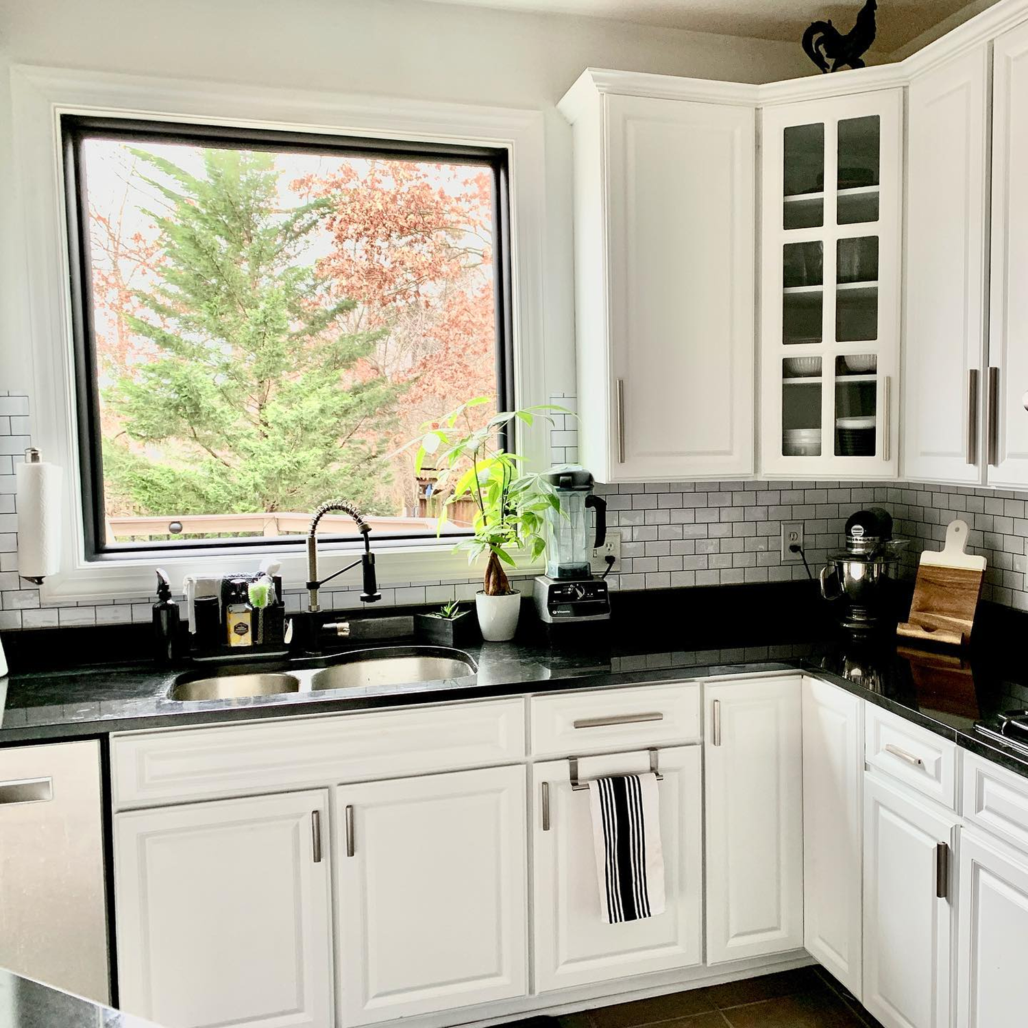 Big black picture window above the sink in a kitchen with white cabinets and black counters.