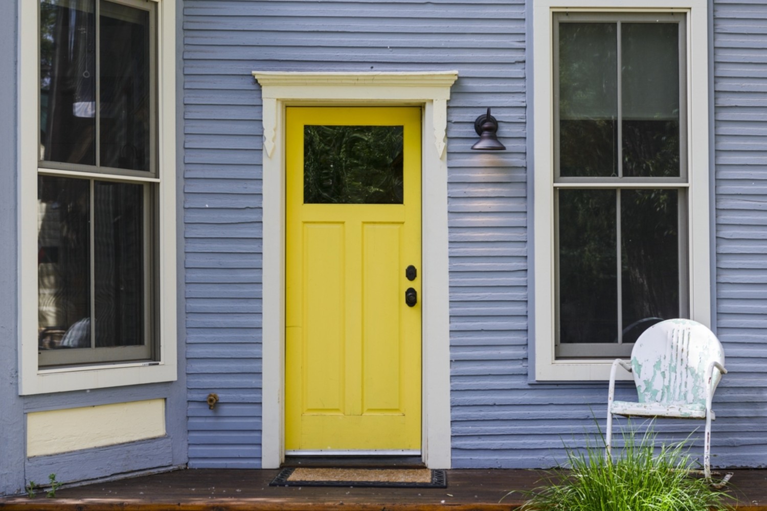 Bright yellow front door with a glass window at the top. The house has light blue siding and white windows.