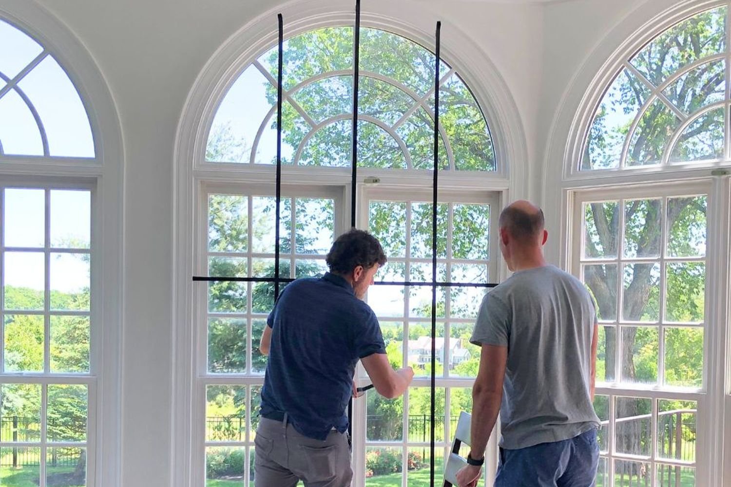 Two men in the mostly remodeled living room holding window grilles.