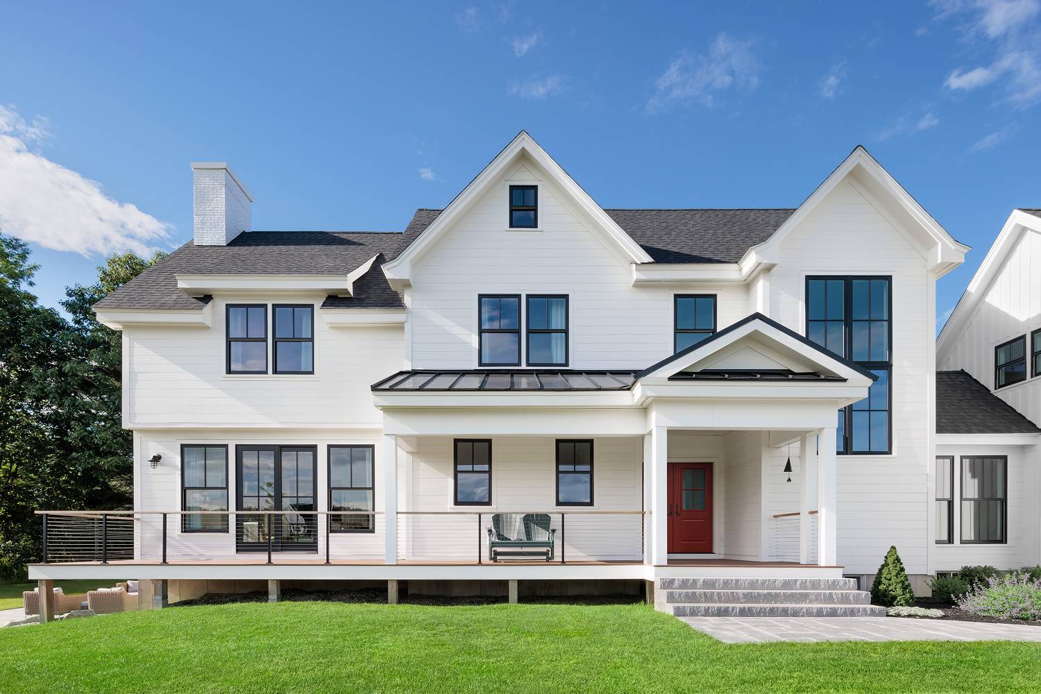 Large white two-story home featuring black-framed replacement windows, expansive floor-to-ceiling window panels, and a bold red front entry door, showcasing modern window and door design with abundant natural light.