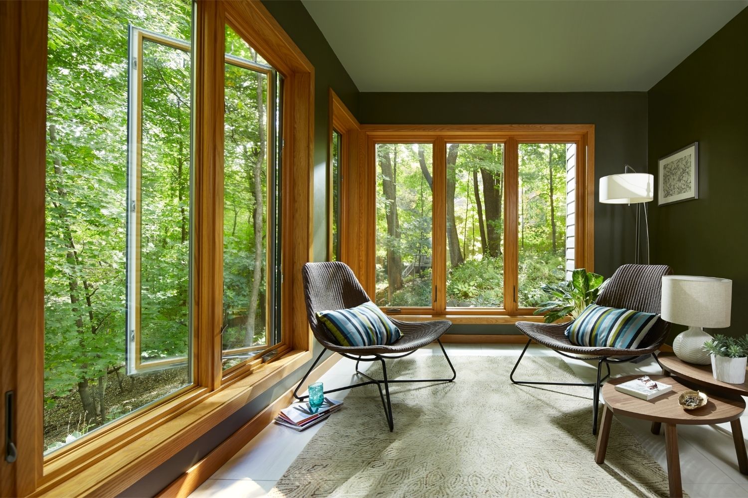 Floor-to-ceiling casement windows in a sitting room that look out on a wooded area.