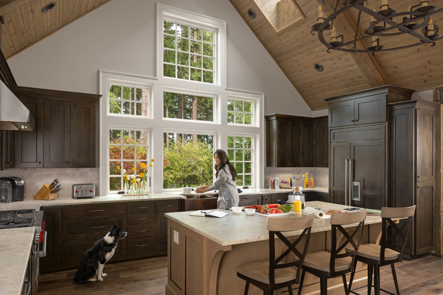 A woman stands in a kitchen, smiling at a dog sitting beside her on the floor.