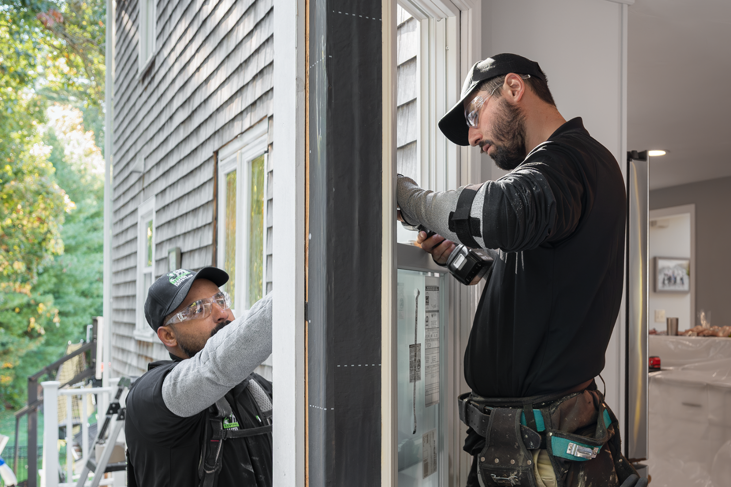 Two men installing a window in a house, focused on their task with tools and materials nearby.