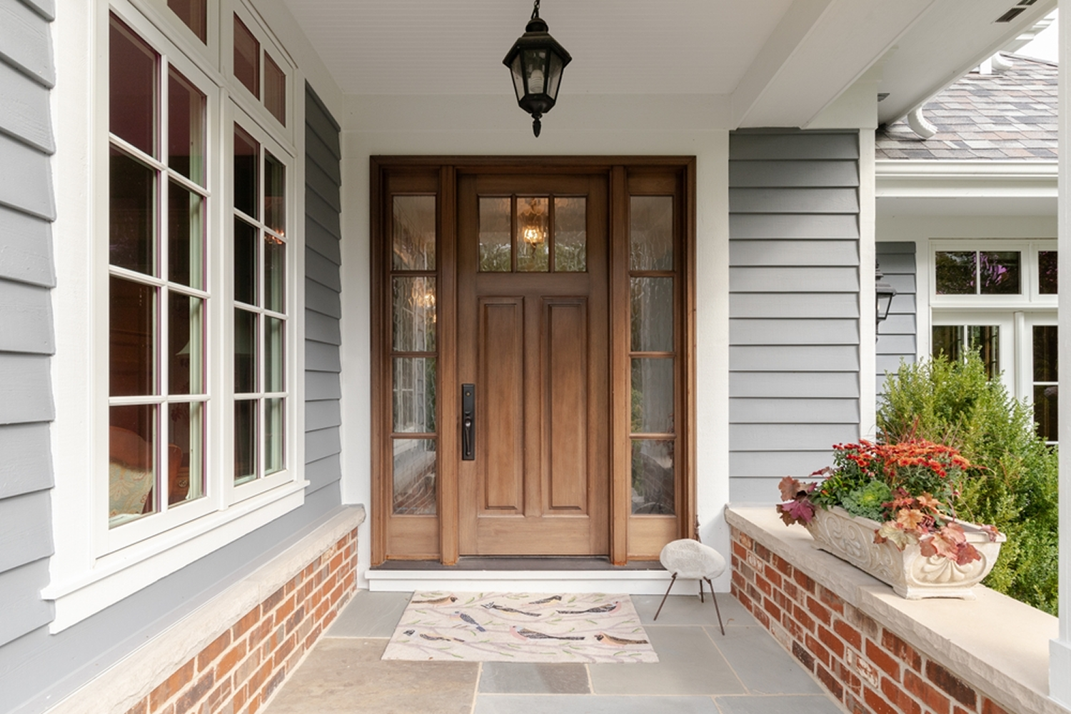 A composite wood entry door surrounded by white trim on a gray house. 