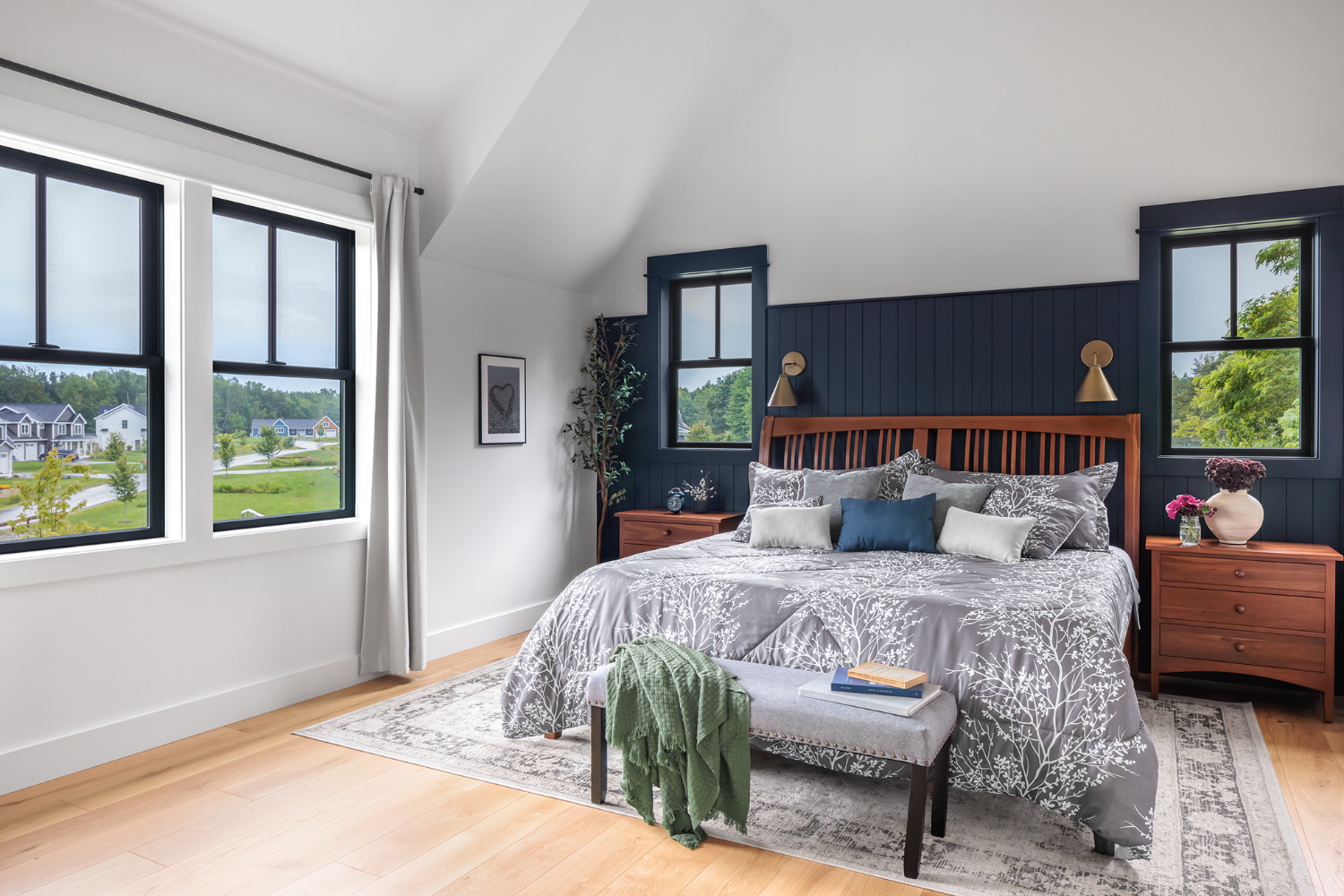 White bedroom with a wood floor and dark blue accent wall with four double hung windows around the room.