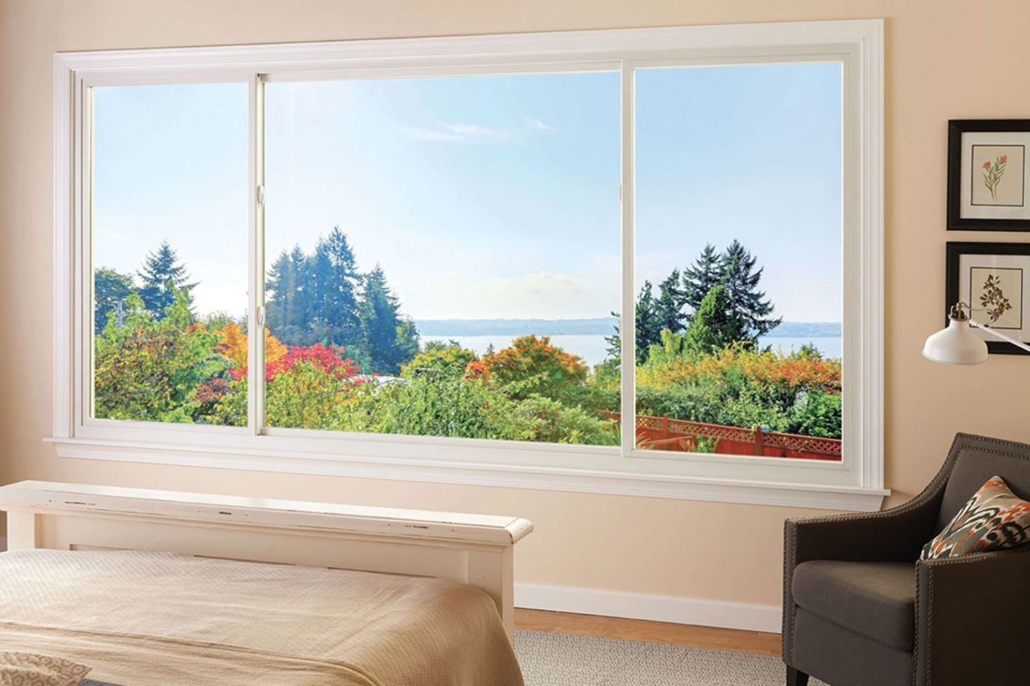Large sliding windows in a bedroom looking over a beautiful fall forest with a body of water in the distance.