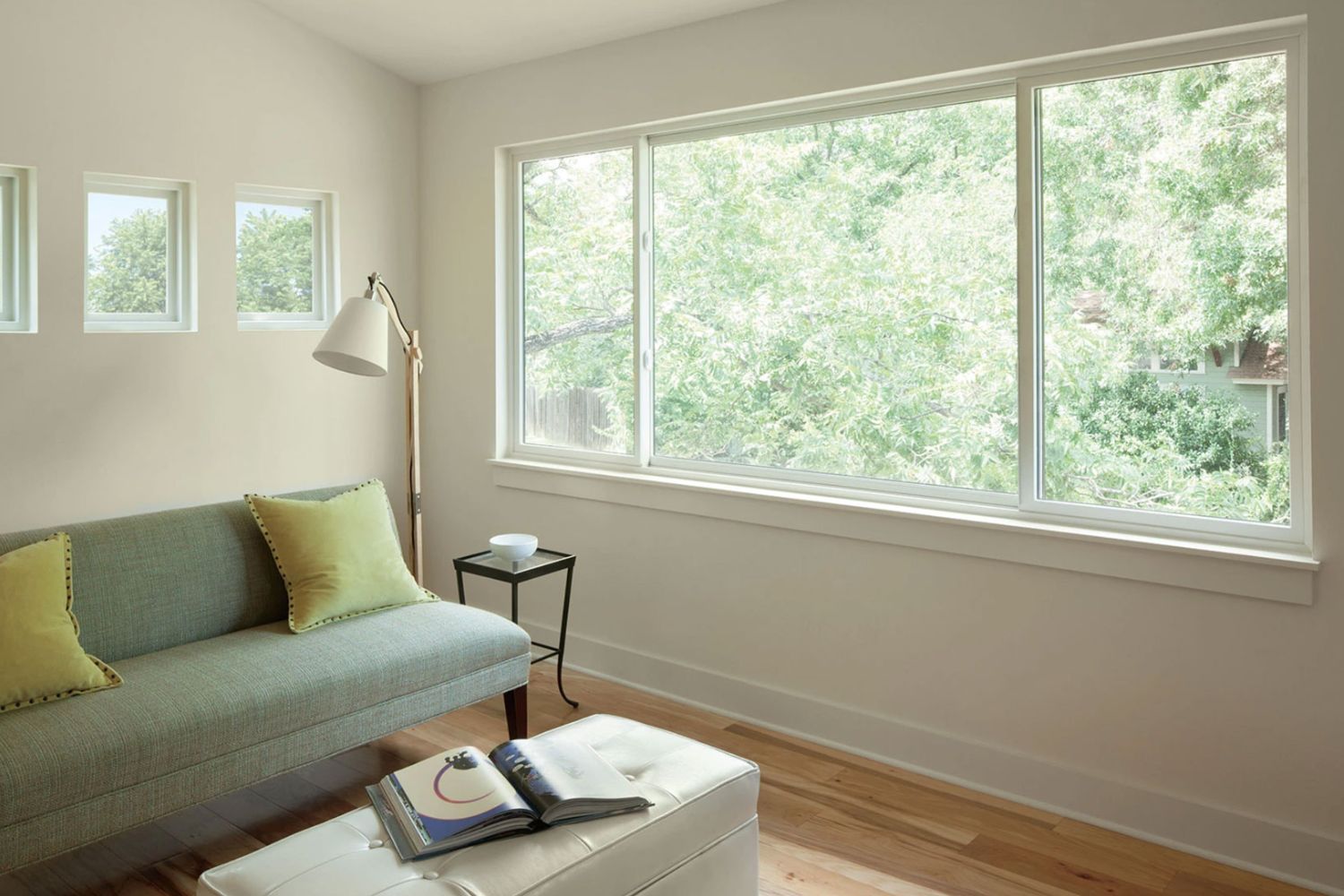 Tan living room with a wood floor and a green couch situated next to a large white sliding window.