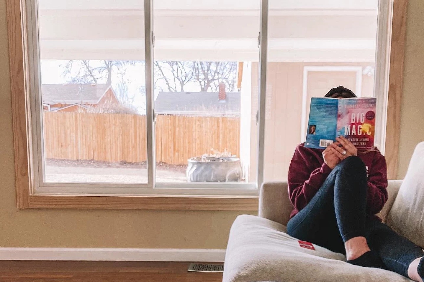 A woman relaxes in front of her Acclaim Sliding window. She reads a book quietly with her dog.
