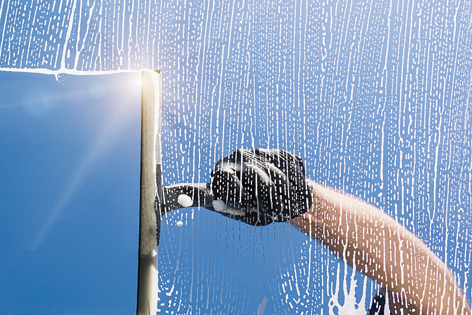 A person cleaning a window in bright sunlight, which you should not do because it leaves streaks.