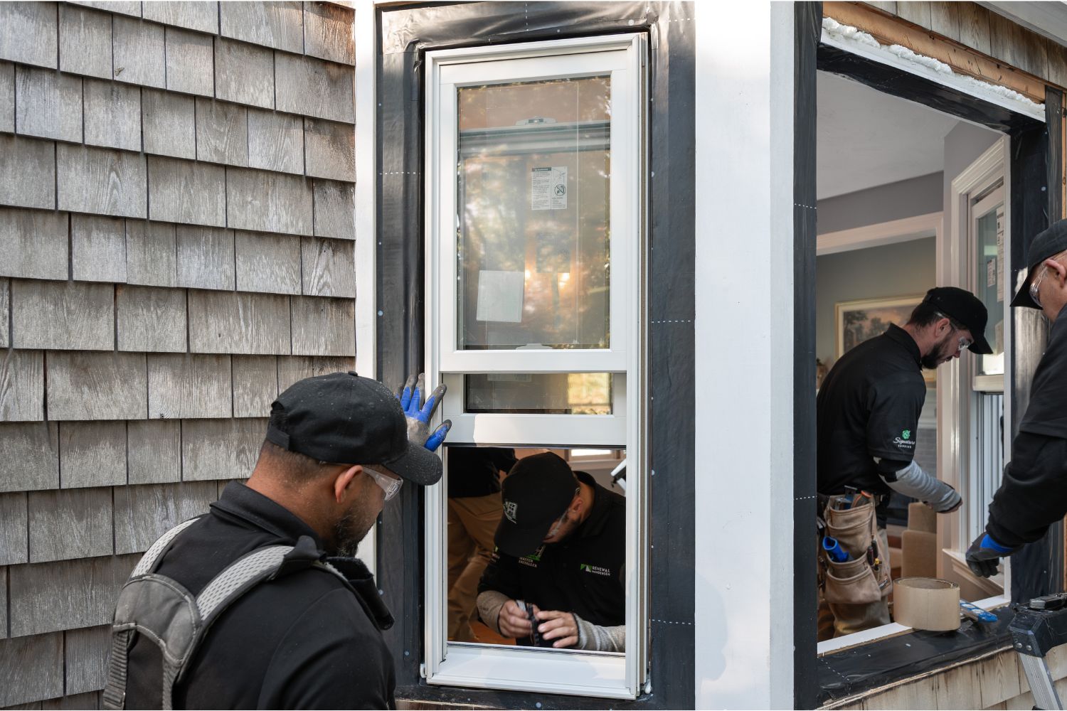 Three men are installing a window in a house, collaborating on the task with tools and materials around them.