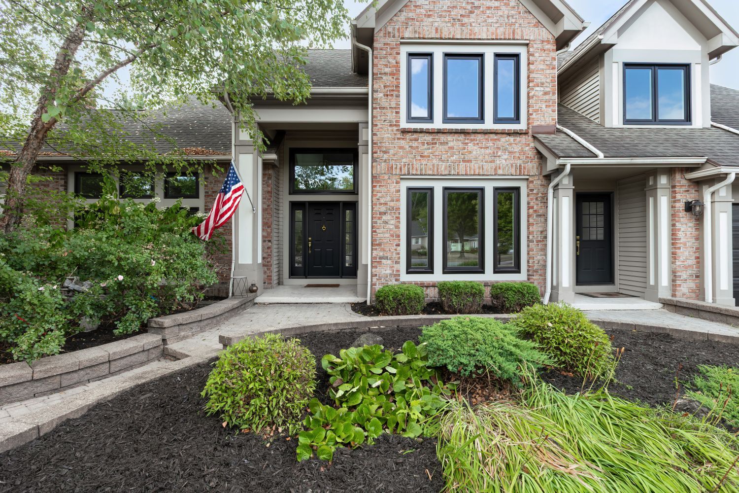 A brick home surrounded by well-maintained landscaping, featuring shrubs and flowers in the front yard.
