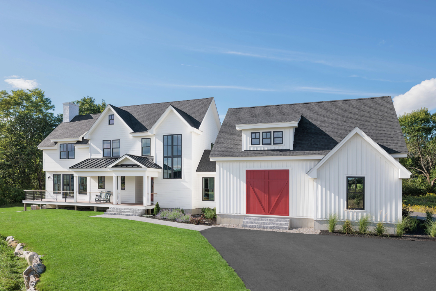 A charming white farmhouse featuring a red door, a driveway, and beautiful composite windows from Renewal by Andersen