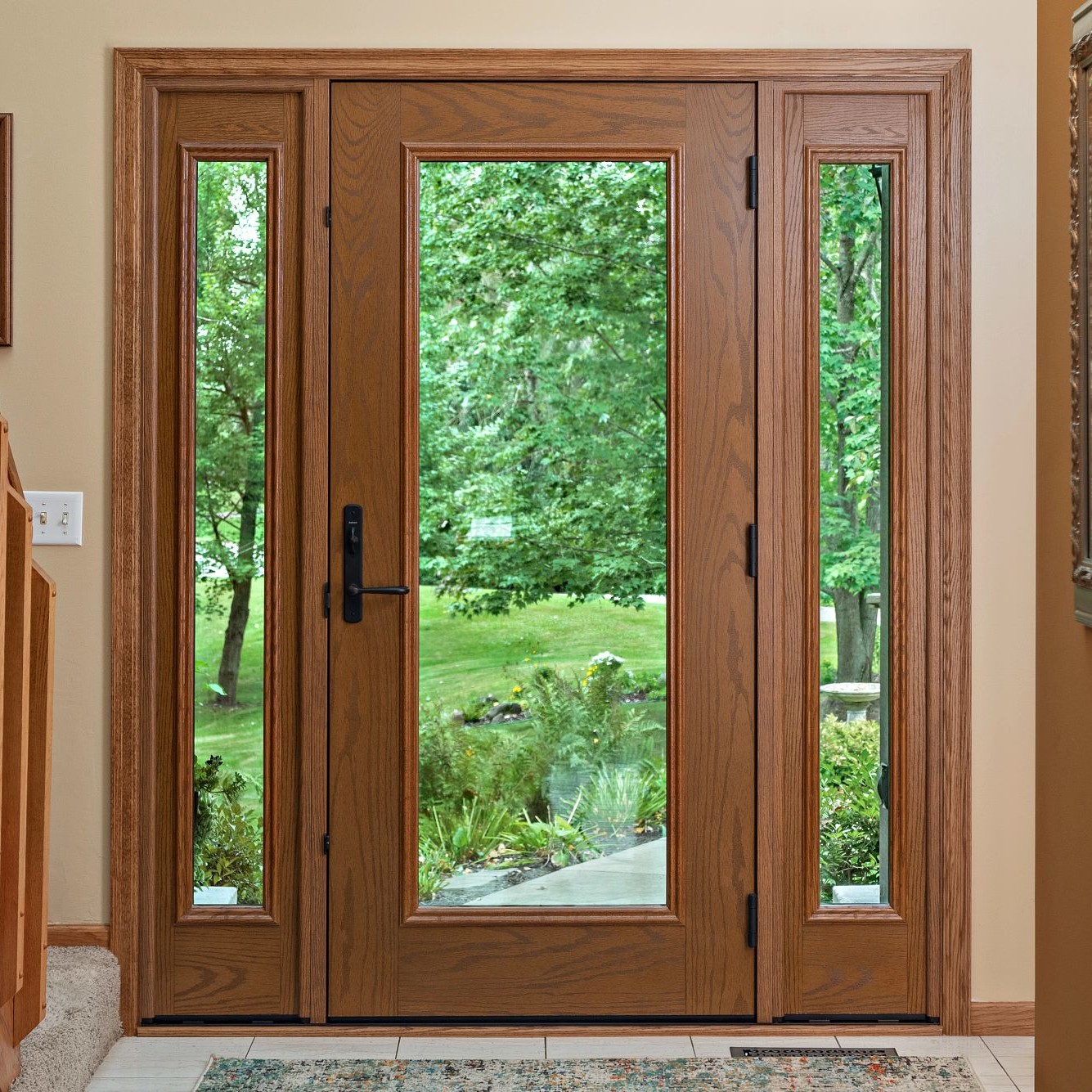 An Ensemble entry door with dual sidelights viewed from inside the home. It is full light with full glass panels. The finish is oak and the hardware is black.