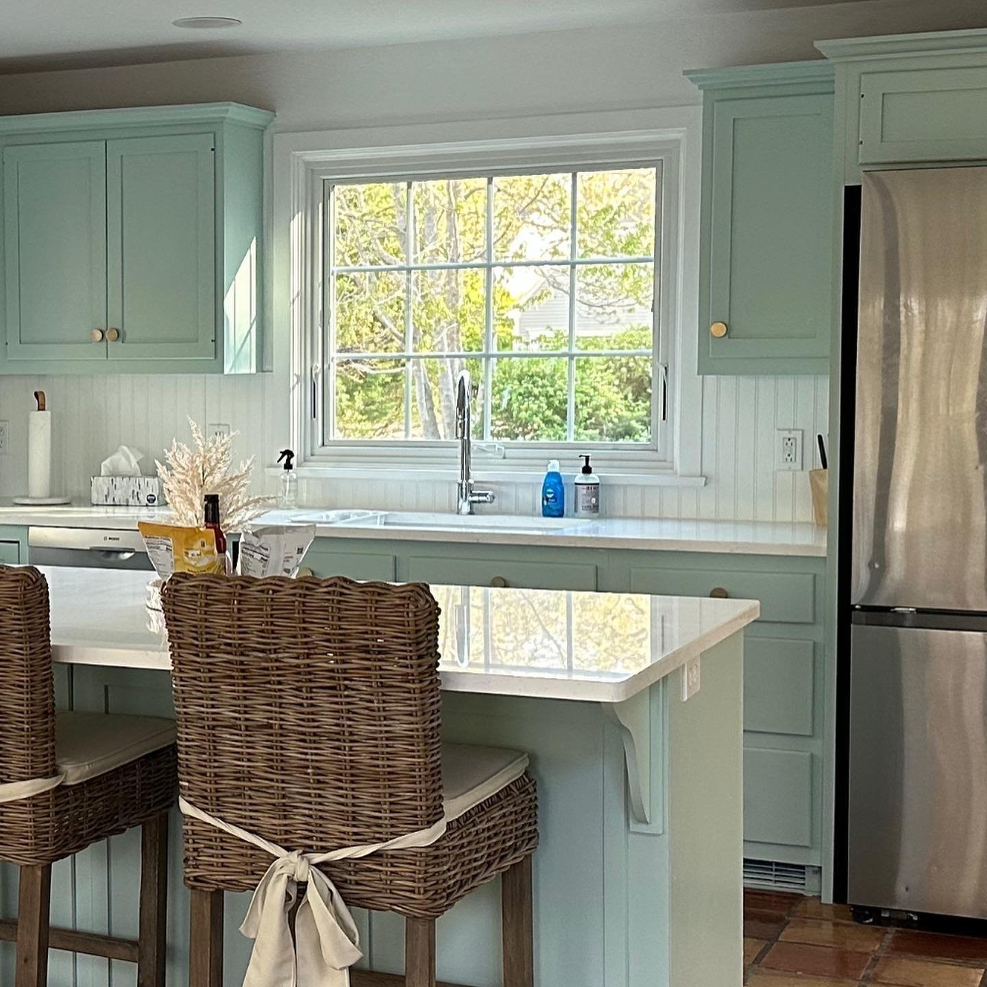 A large awning window in a kitchen with teal cabinets and quartz countertops.