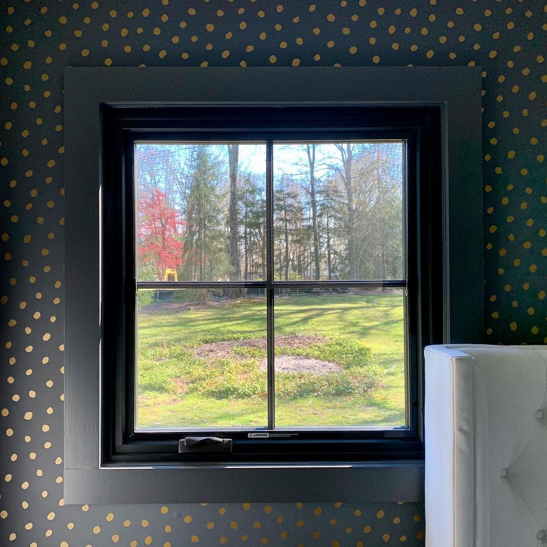 A square casement window with equal light grilles in a bedroom with dark green wallpaper.