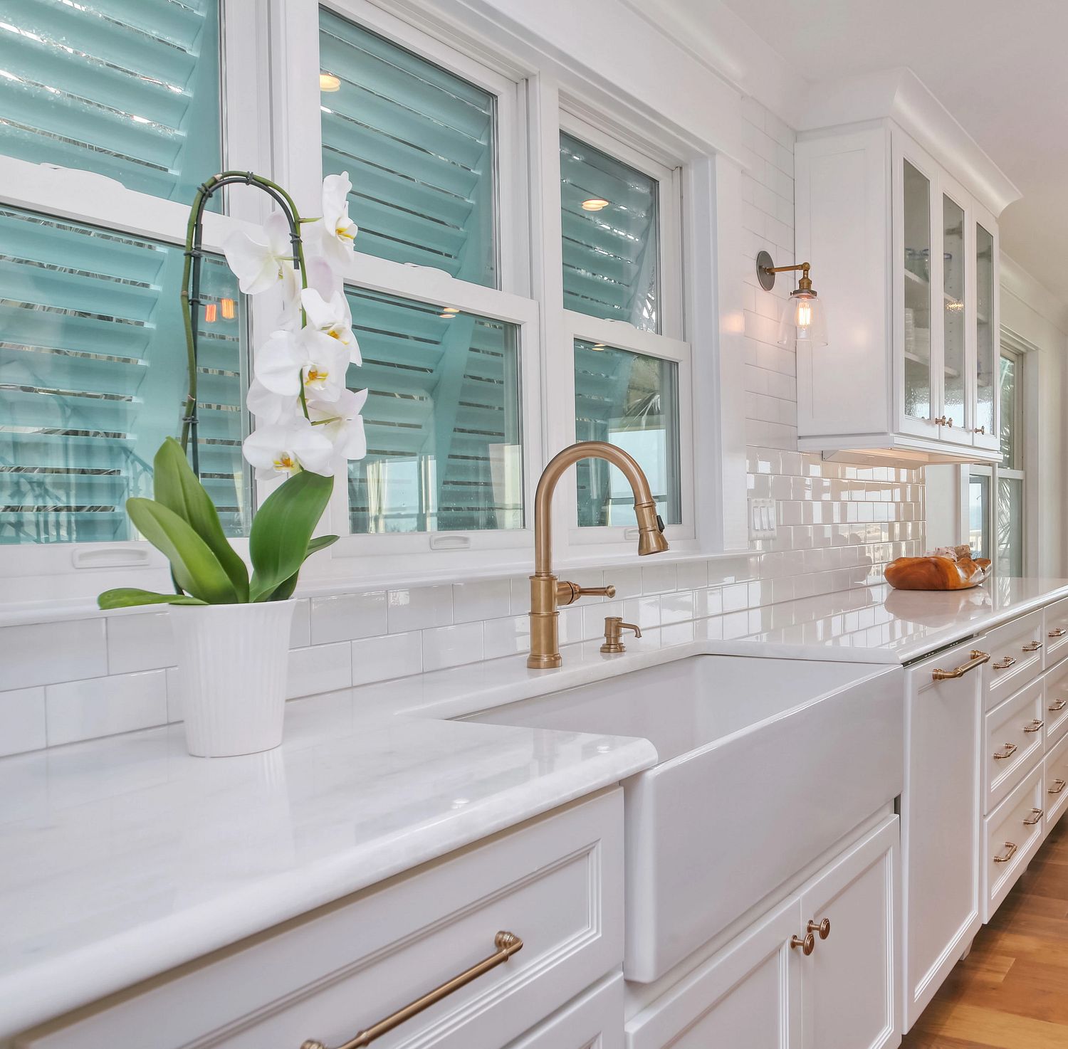 A kitchen with white granite counters and a gold faucet. The windows have hurricane shutters..
