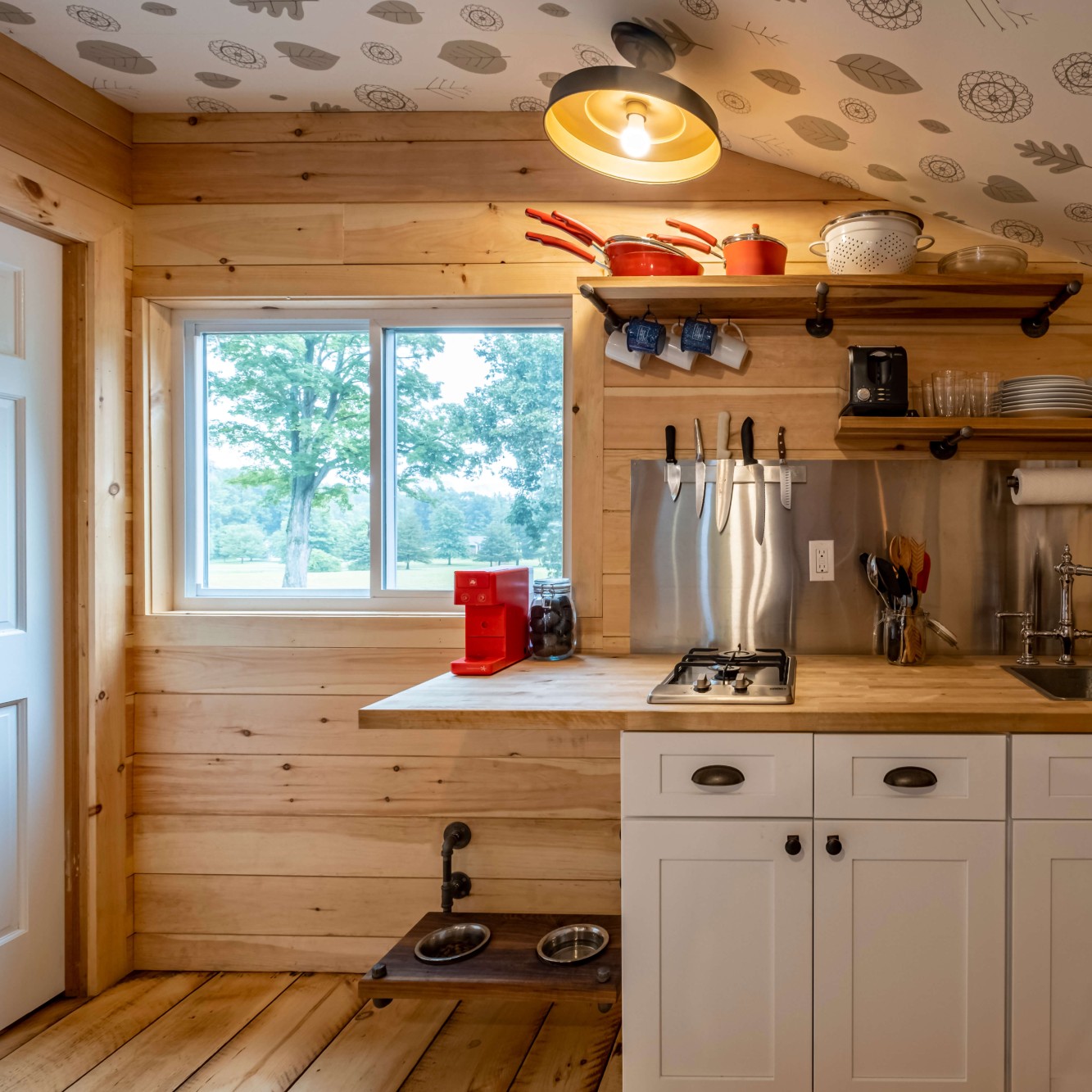 The kitchen in a guest apartment or carriage house on a property in the New York mountains.. It has knotty pine paneling and a gliding window.
