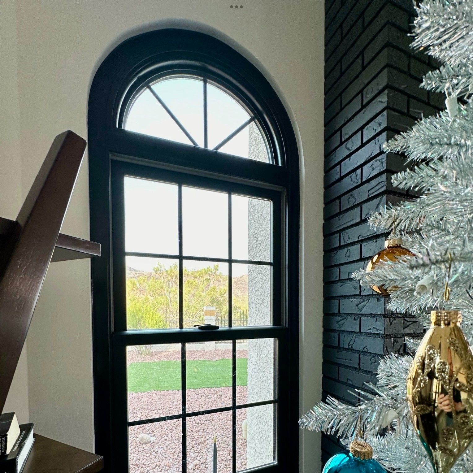 A black double-hung window topped with a circle top window. There is a Silver flocked Christmas tree near by.