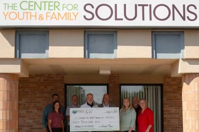Group of individuals stand outside of "The Center For Youth And Family" building with an oversized donation check.